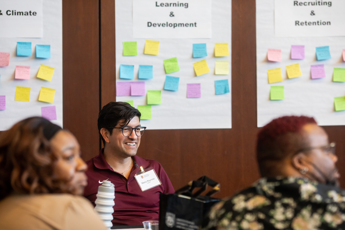 Faculty and staff sit at a table in front of a wall with post it notes